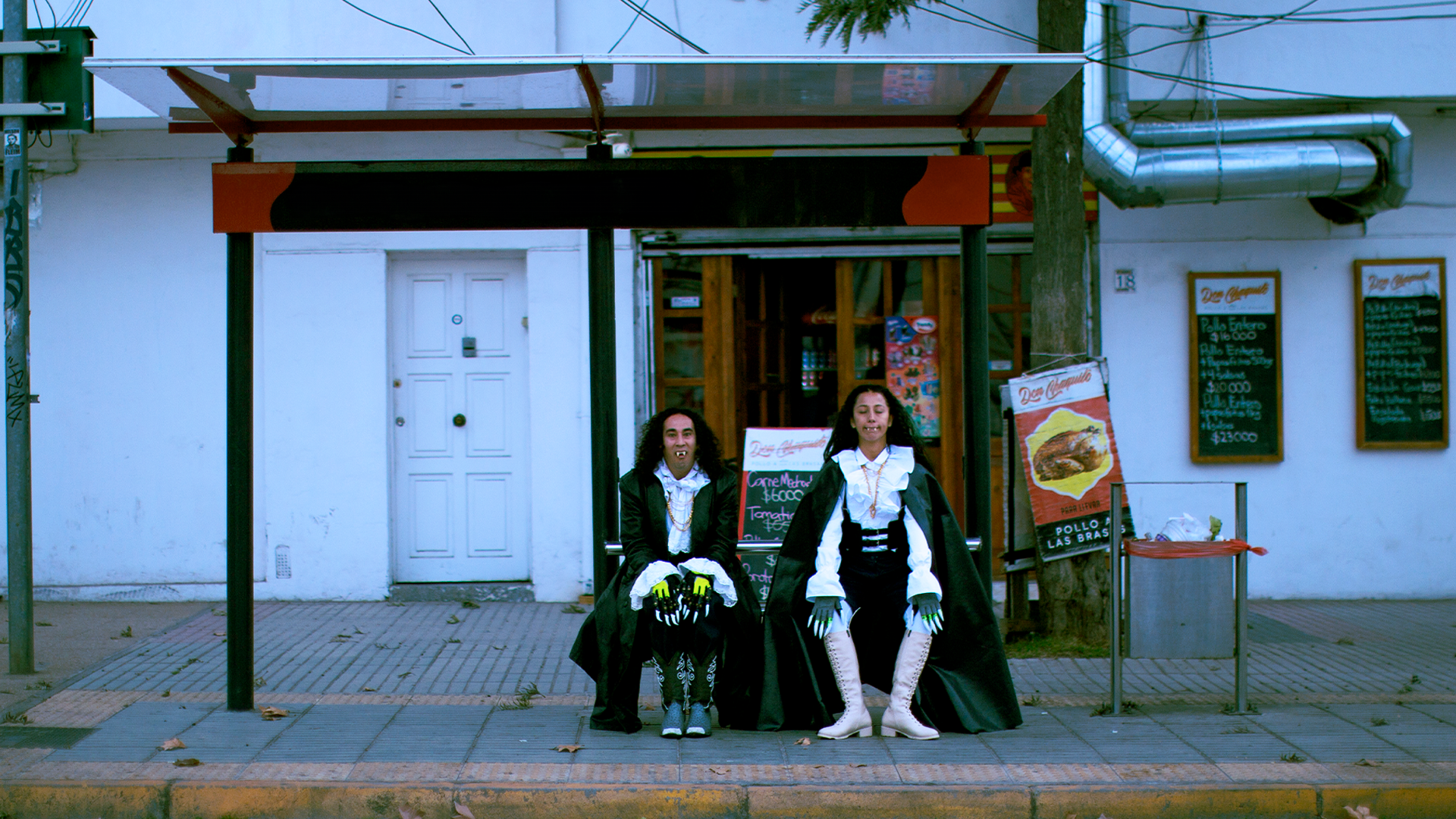 Two people dressed in vampire costumes are sitting at a bus stop