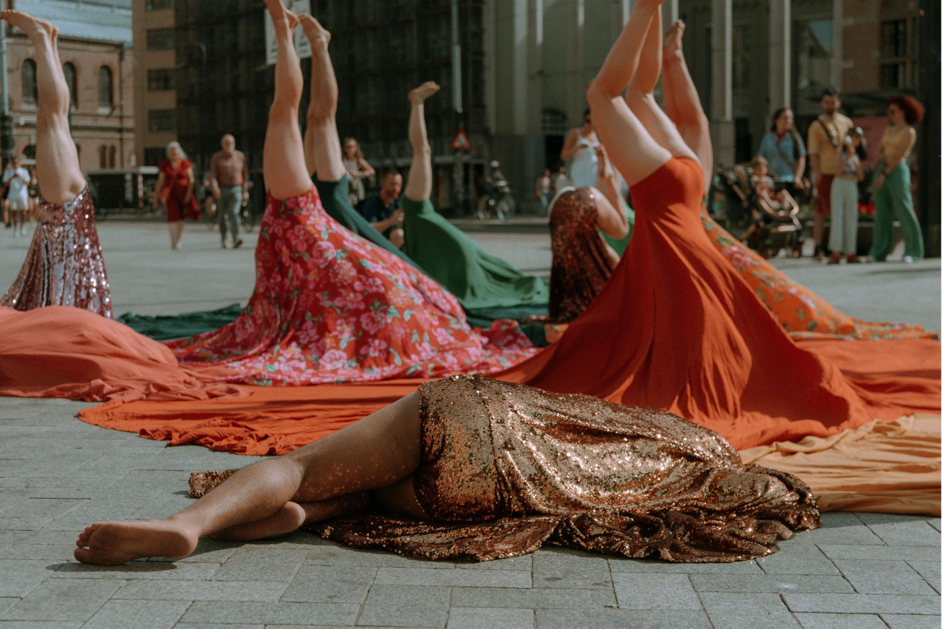 Une personne est allongée au sol, sa jupe par dessus la tête. Derrière elle, d'autres tiennent la posture du poirier.