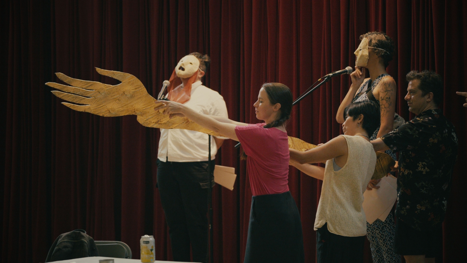 Des participants tiennent une grande main en or alors que des personnes avec des masques en papier parlent.