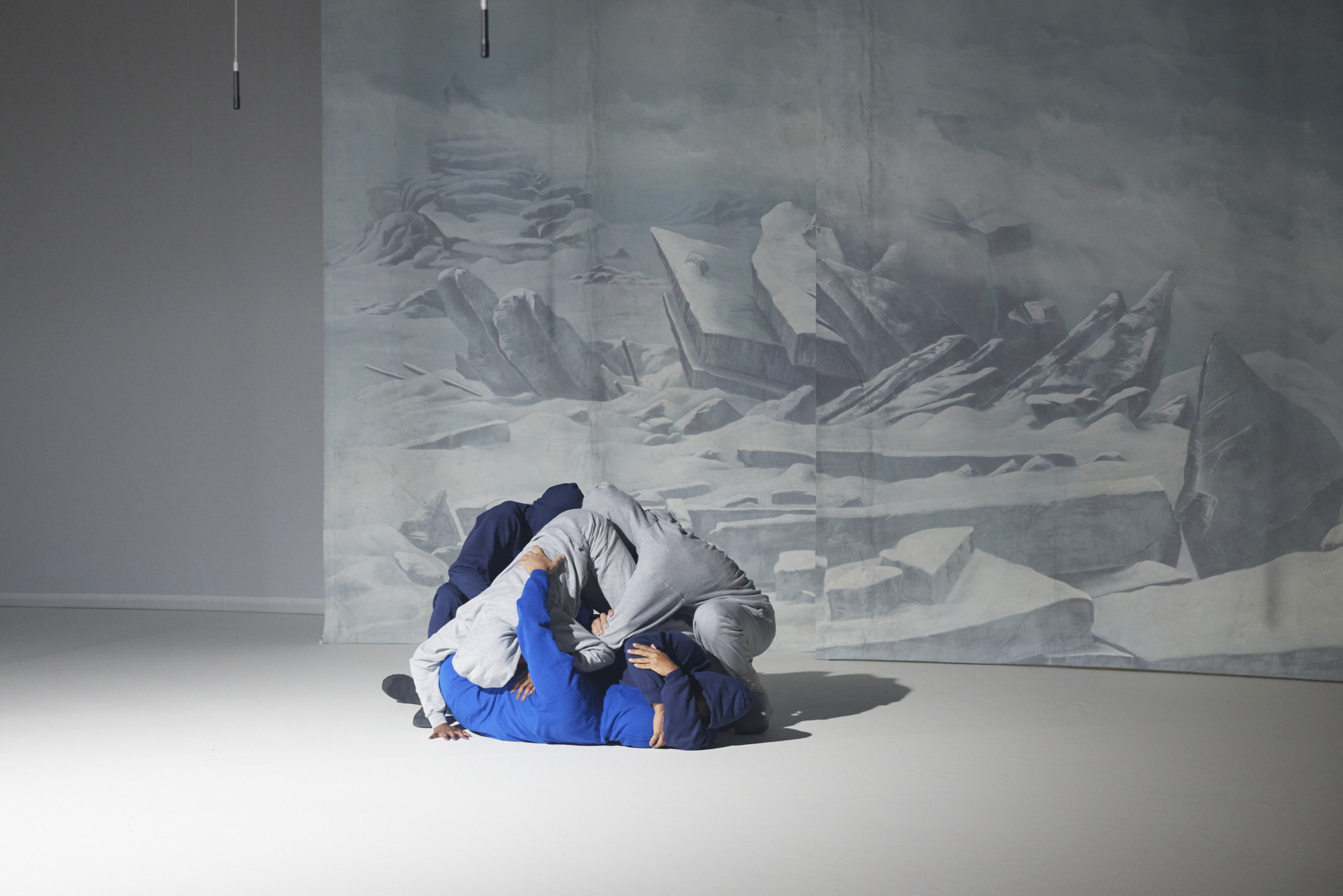 Des danseurs et danseuses forment une pyramide au sol en entremêlant leurs corps, faisant écho à une image de montagnes très blanches en fond de scène.
