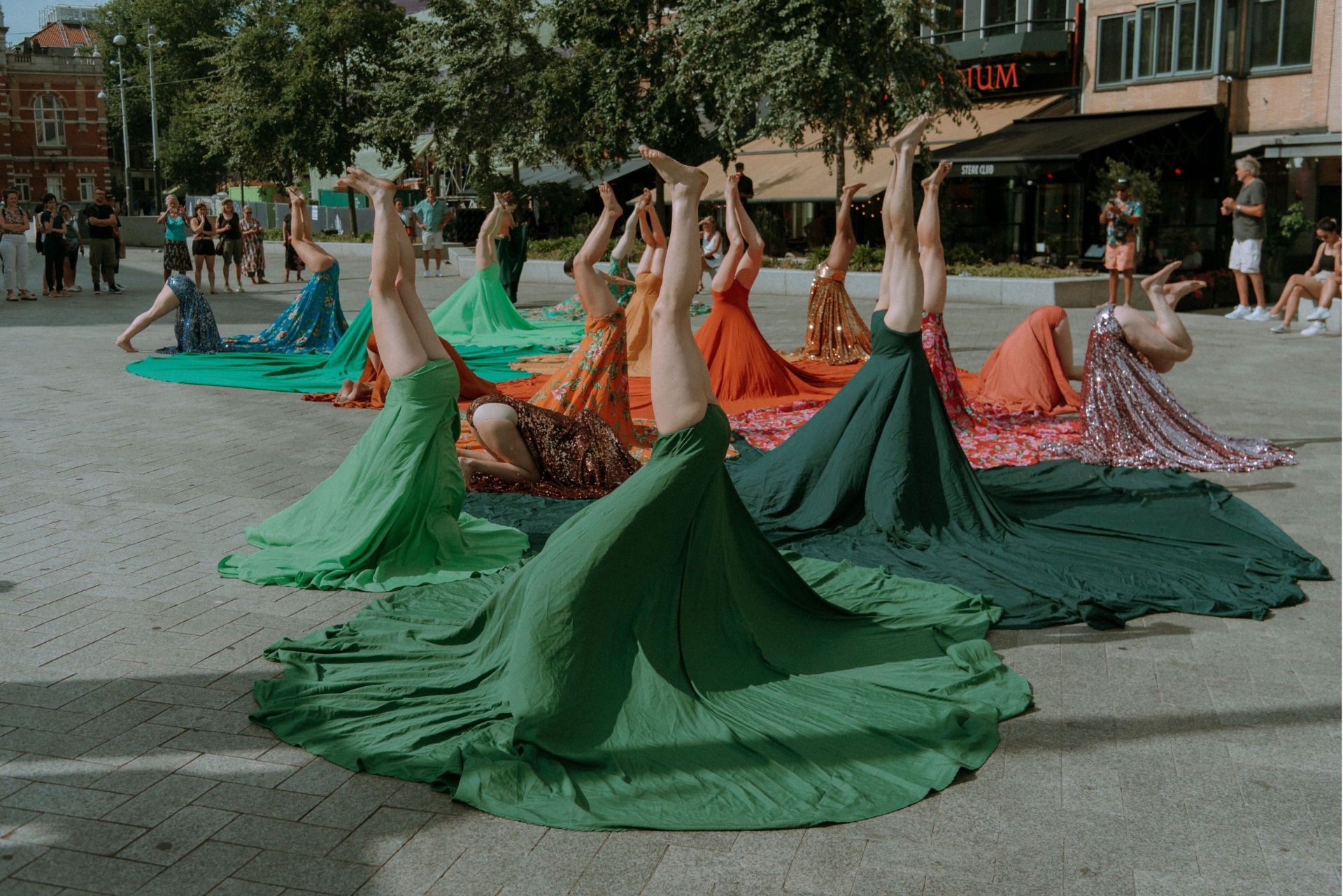 Plusieurs personnes tiennent la posture du poirier. Leurs troncs sont recouverts par de grandes jupes colorées.