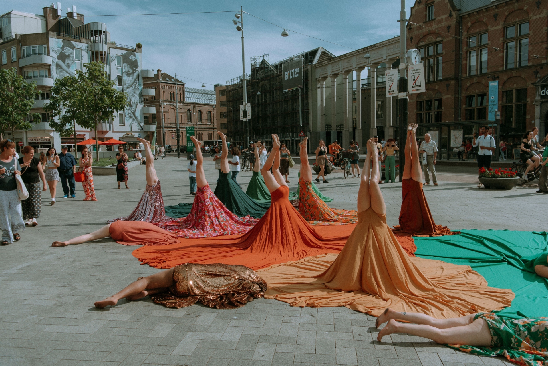 Plusieurs personnes tiennent la posture du poirier et d'autres sont allongées au sol. Leurs troncs sont recouverts par de grandes jupes colorées.