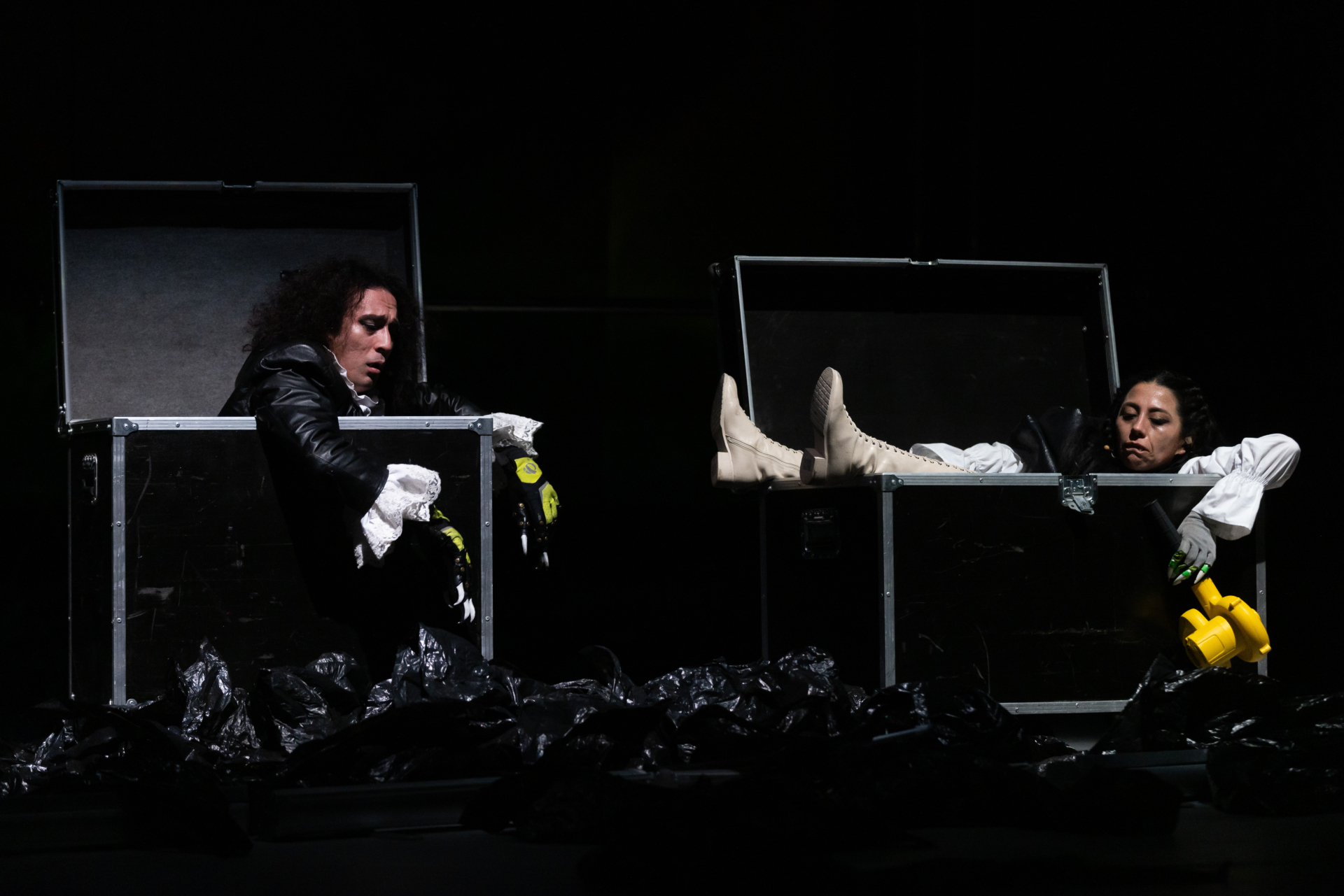 Deux personnages avec des griffes aux doigts et vêtus de chemise avec des manches bouffantes sortent chacun d'une grande malle noire et métallique utilisée ranger du matériel lors d'événements