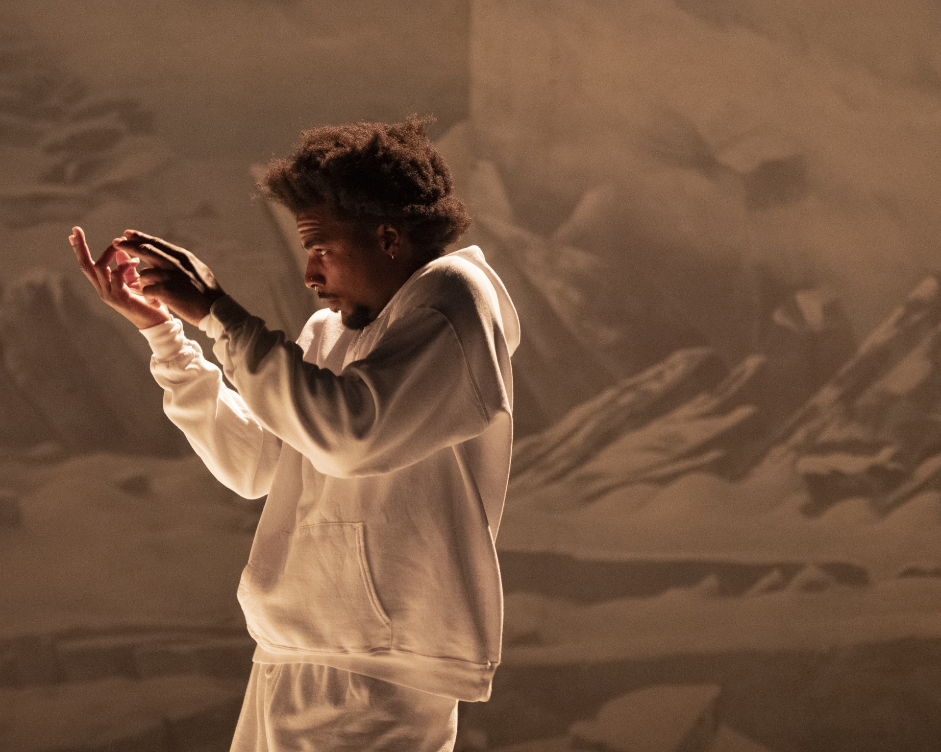 Un danseur vêtu d'un survêtement blanc évolue devant un décor représentant des montagnes, les bras levés.