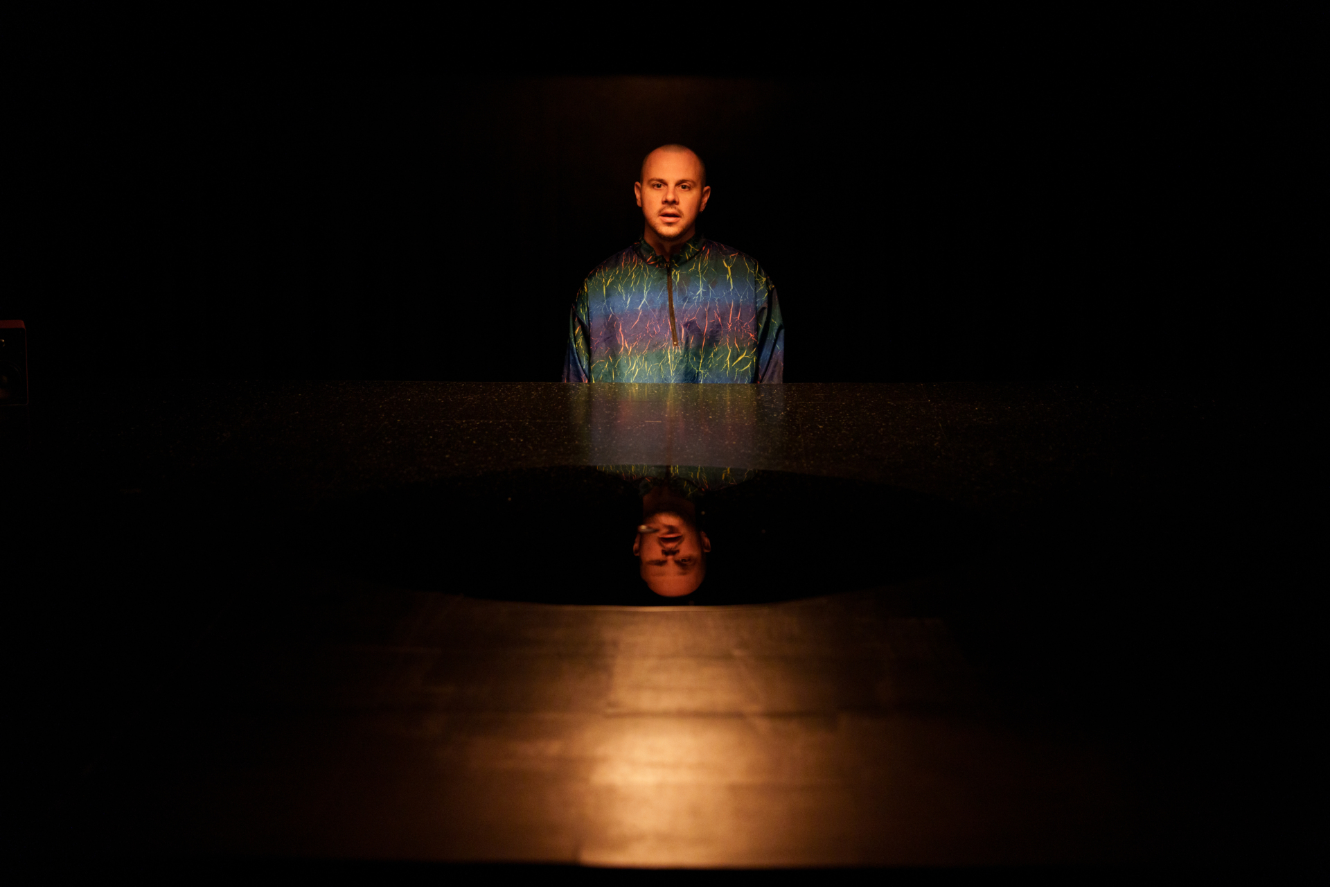 Un homme debout avec un imperméable multicolore se tient au-dessus d'une surface lisse qui réfléchit son visage.