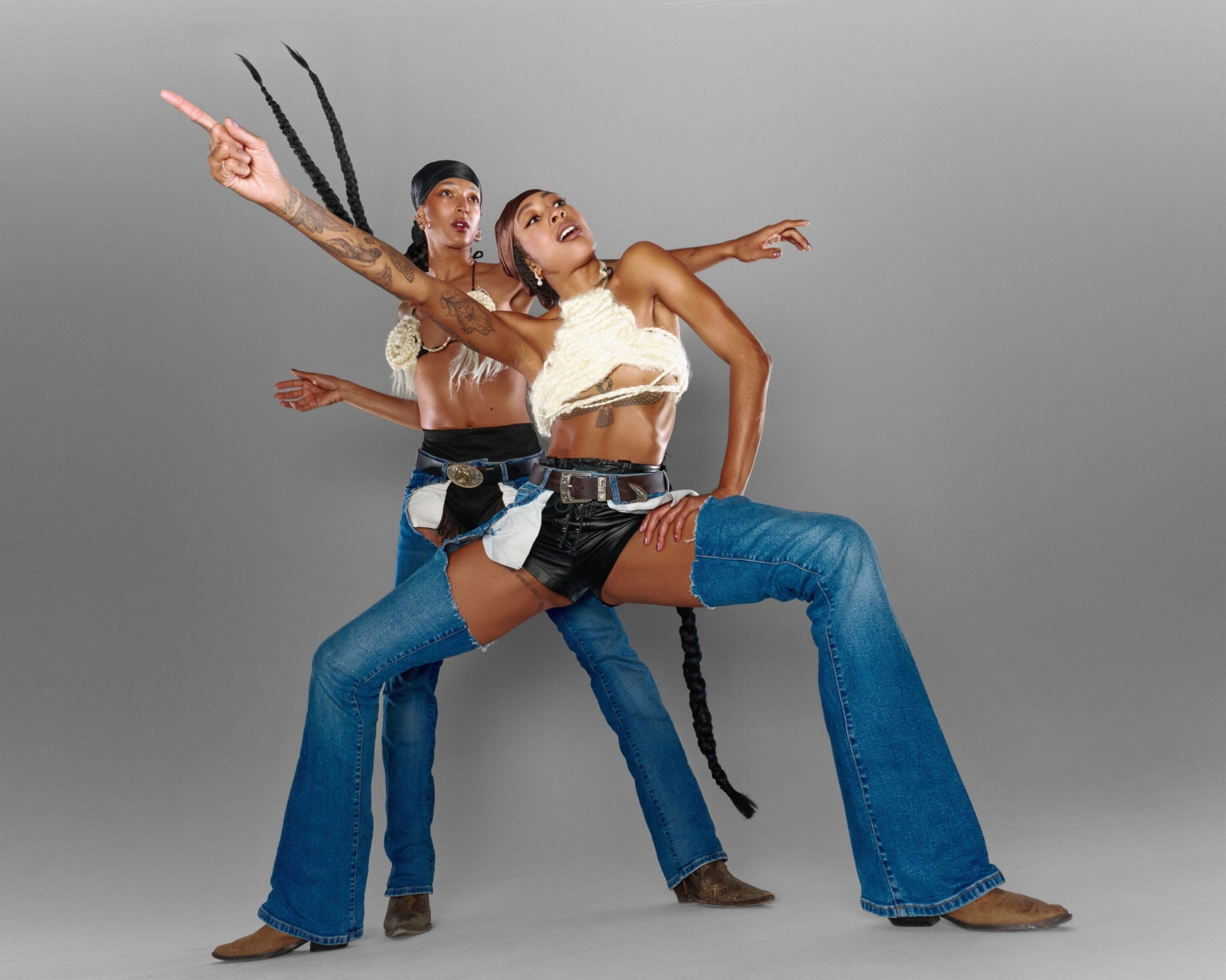 Photo prise en contre-plongée 
Stacey en grand pilé en 2e position regarde vers la droite et pointe vers la gauche. Satinée se trouve derrière elle, tresses dans le vent, les bras allongés dans l'espace, regardant au loin.