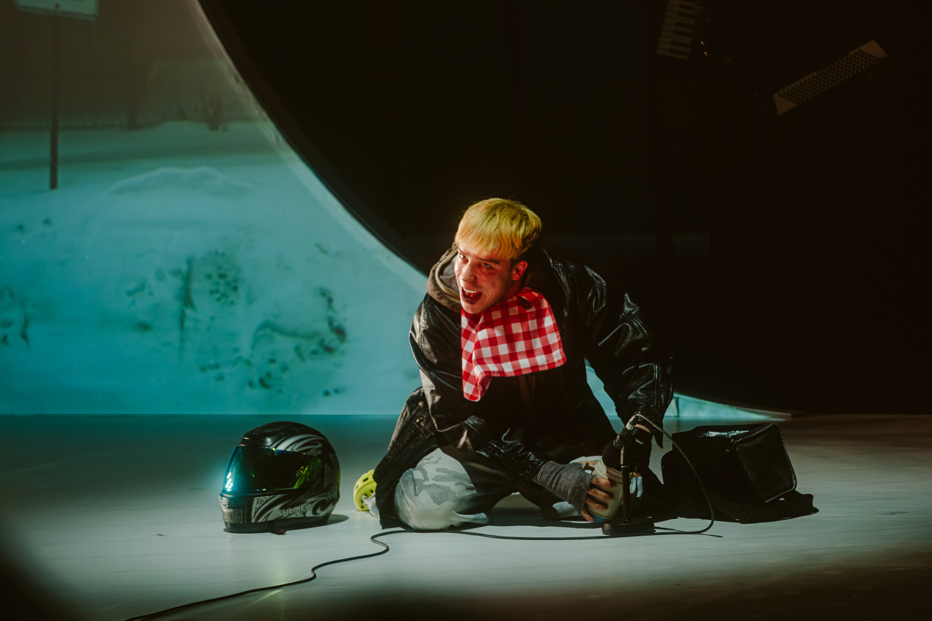 A blond man kneels on stage, making sound effects.