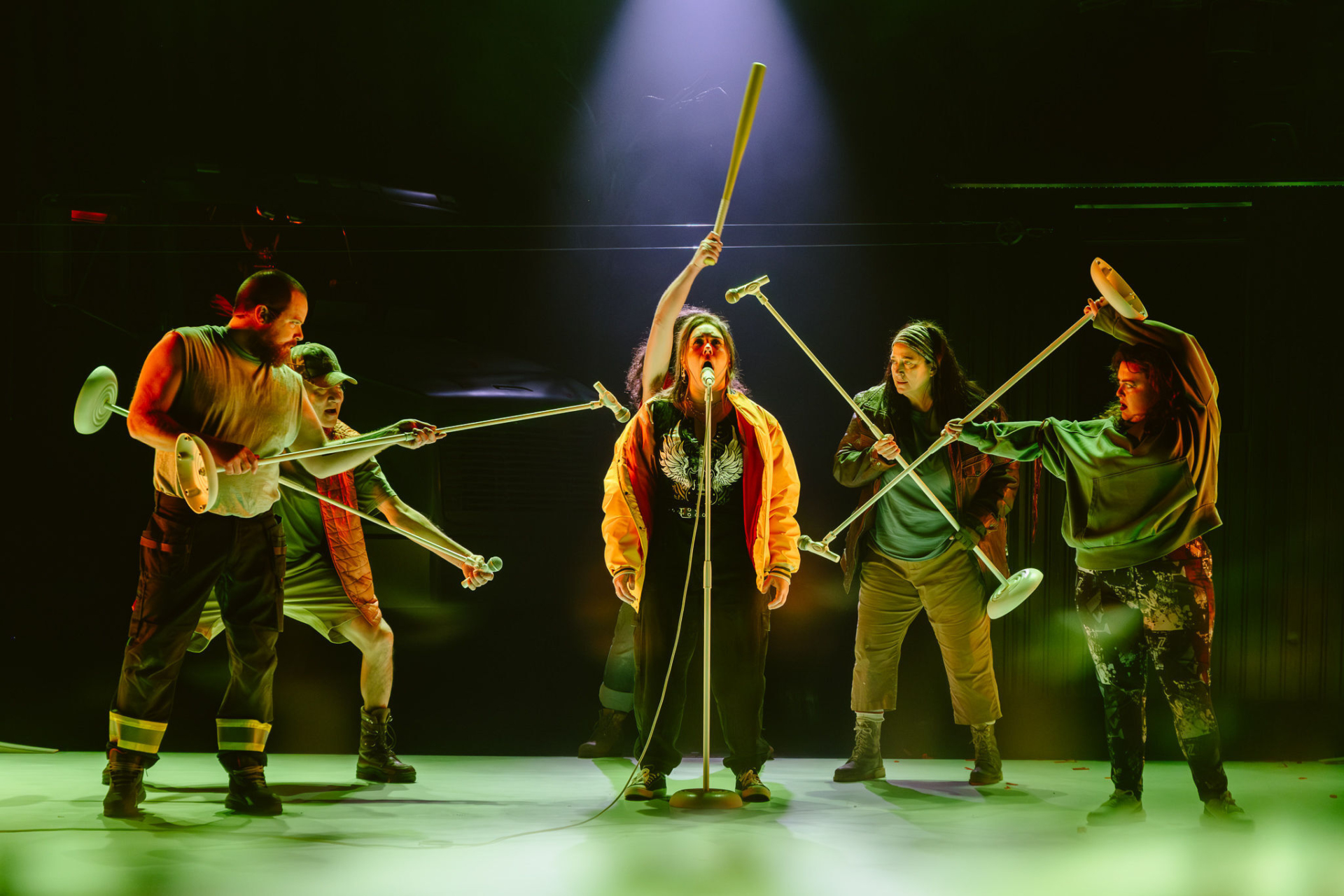 Several characters from the novel Querelle de Roberval are gathered behind Jezabel, who is speaking into a microphone, each holding a microphone stand pointed toward her.
