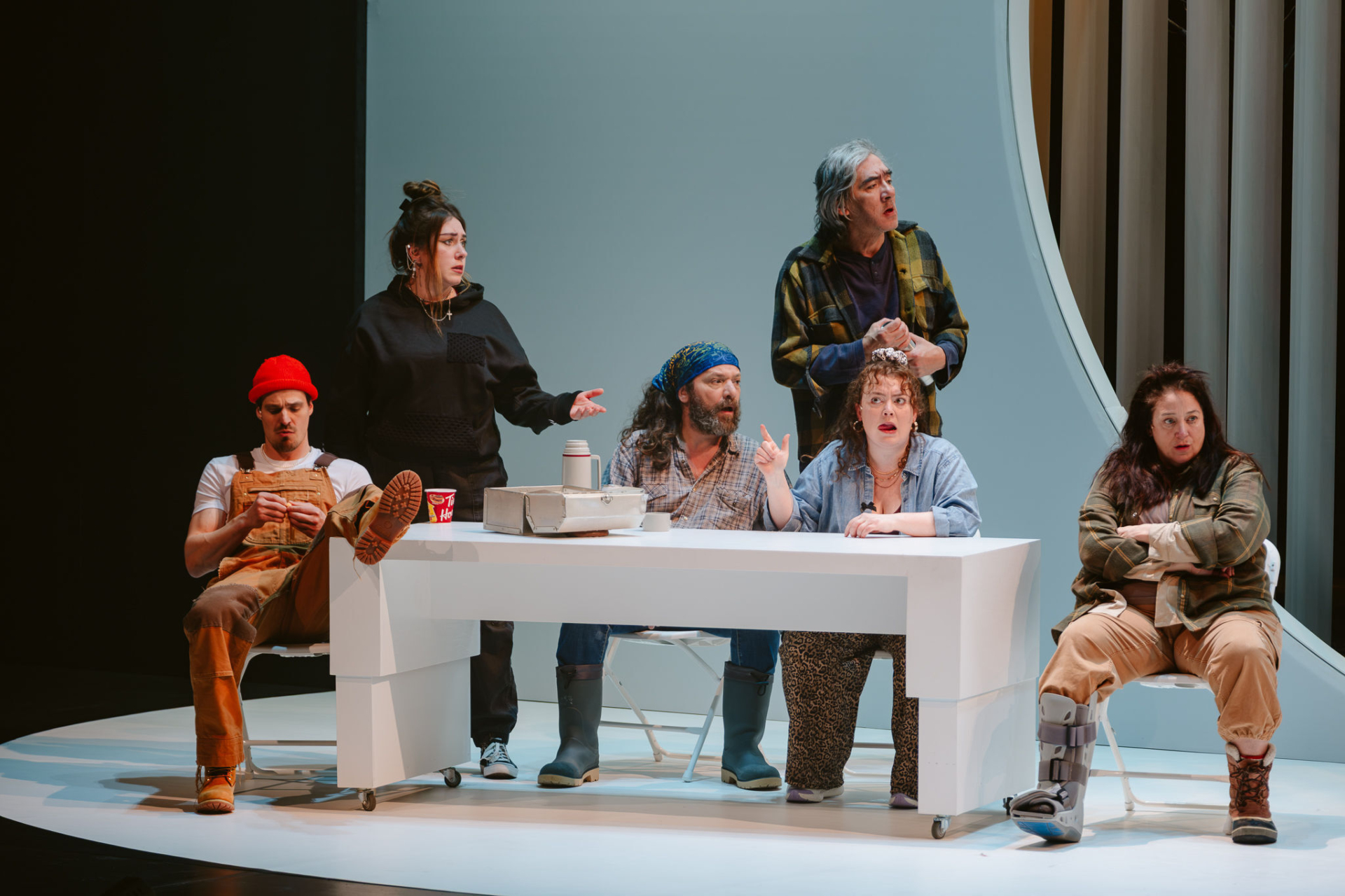 Several characters from the novel Querelle de Roberval are sitting at a table drinking coffee and looking unhappy.