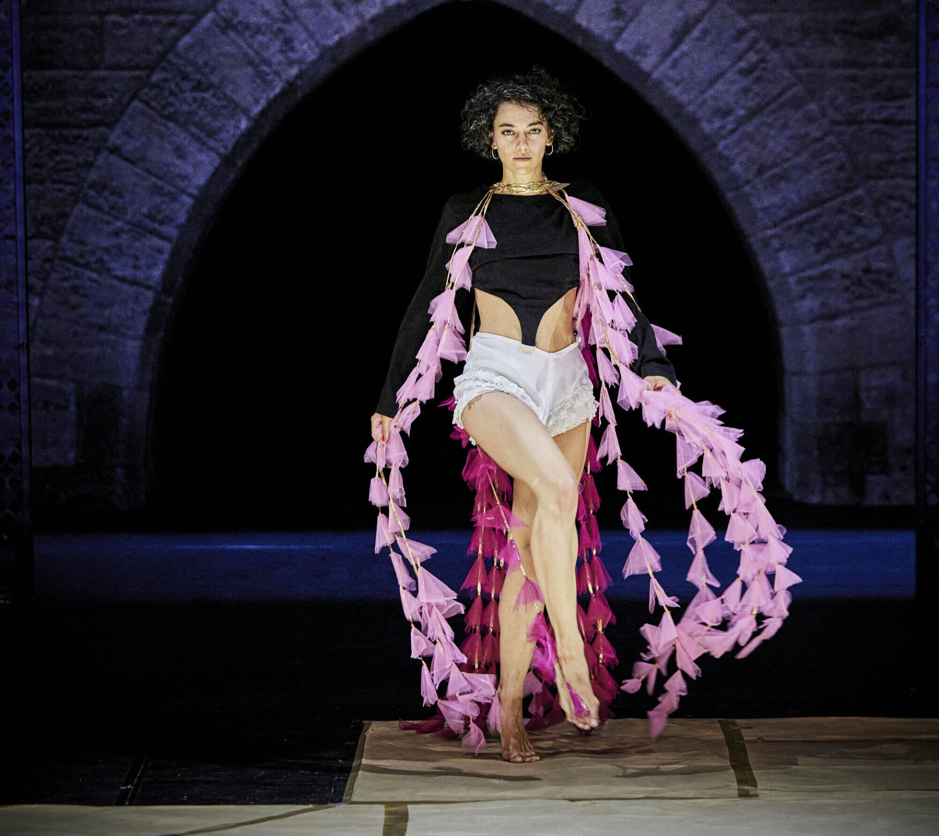 An interpreter walks as if in a fashion show, wearing large pink scarves.