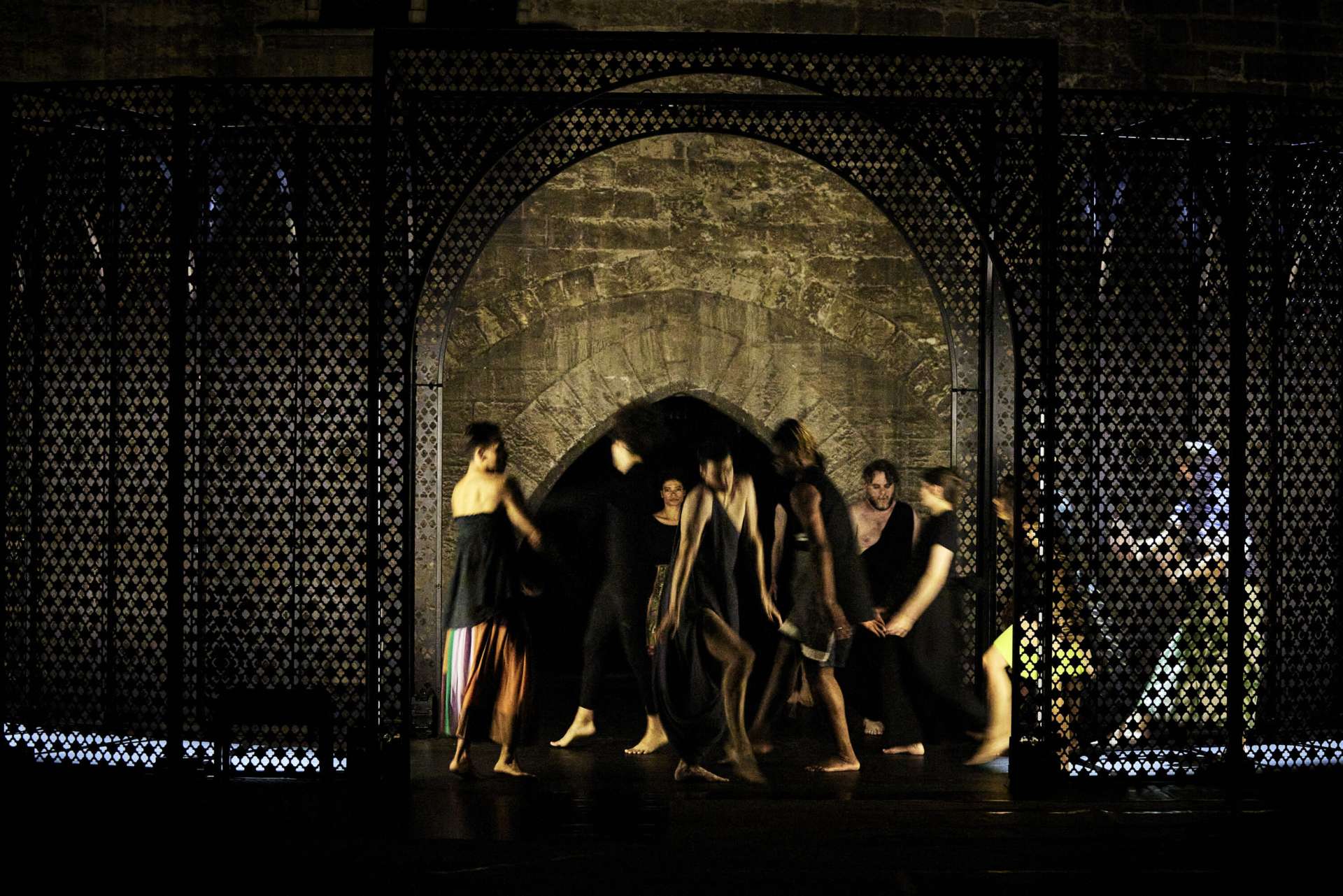 Several performers dressed in black can be seen dancing between two mashrabiya screens.