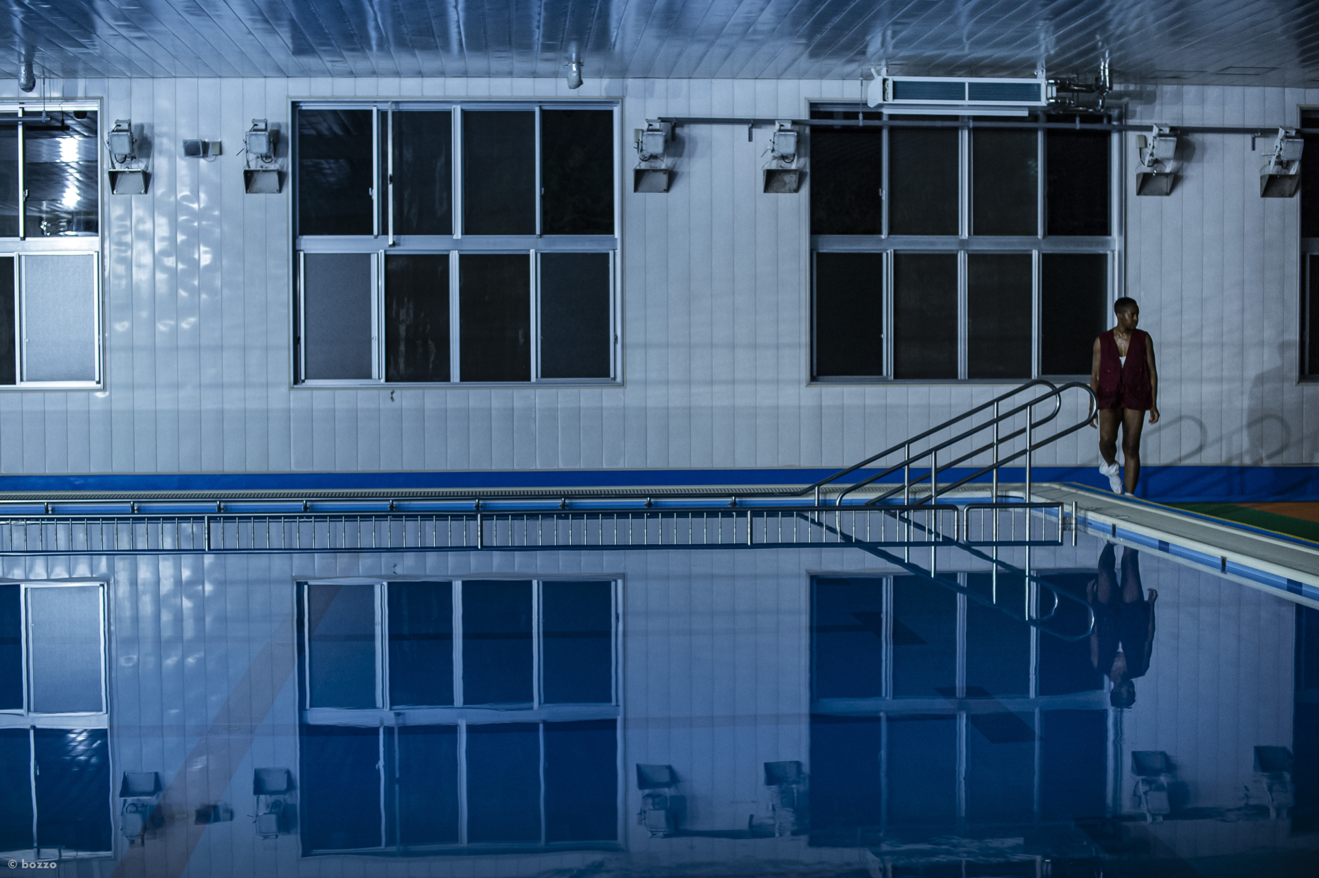 Dana Michel s'approche d'une piscine municipale intérieure faiblement éclairée.