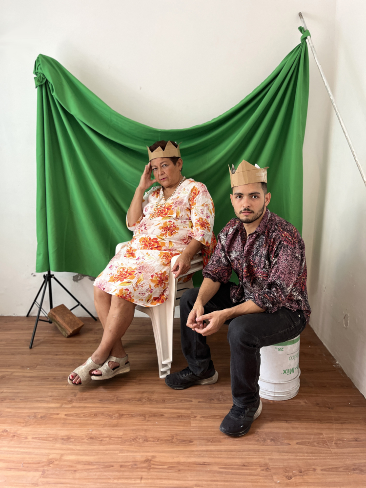 Anacarsis Ramos and his mother are sitting in front of a green background wearing paper crowns.