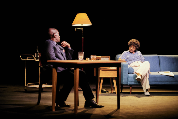 James Baldwin (Greig Sargeant) assis à son bureau discute avec Lorraine Hansberry (April Matthis) assis sur le canapé.