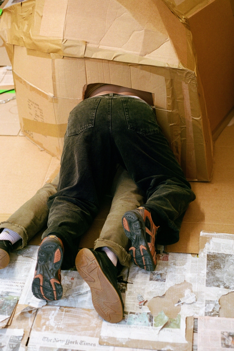 Deux corps sont allongés l'un sur l'autre, leurs troncs dissimulés par un boite de carton.