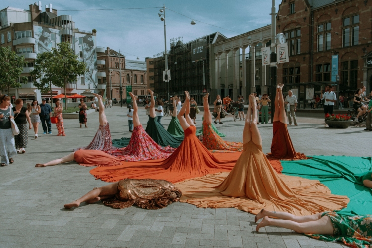 Plusieurs personnes tiennent la posture du poirier et d'autres sont allongées au sol. Leurs troncs sont recouverts par de grandes jupes colorées.