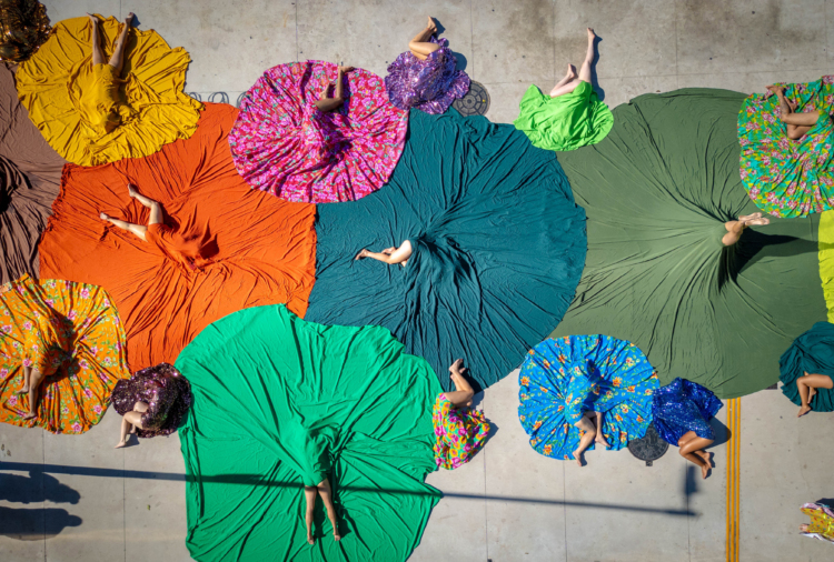 Vue aérienne de personnes tenant la posture du poirier alors que d'autres sont étendues au sol. Chaque personne se trouve au centre d'un grand cercle de couleur créé de tissus.