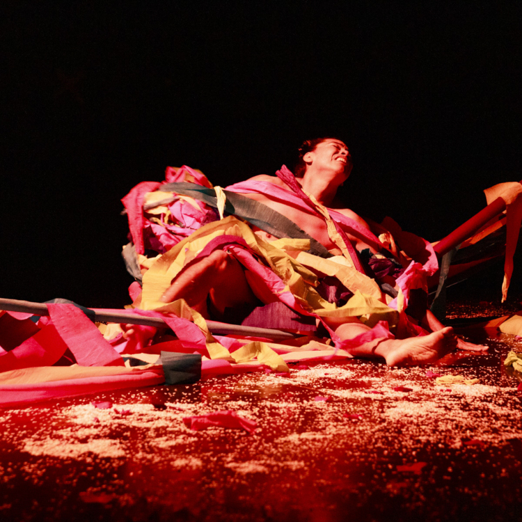 Lukas Avendaño est assis à terre, éclairé par de la lumière rouge et ensevelli sous des rubans de tissu.