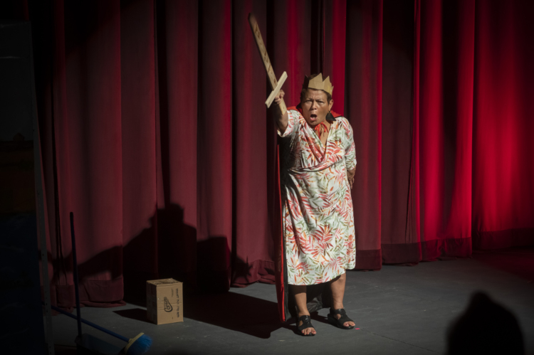Josefina Orlaineta brandishes a wooden sword with a crown on her head in front of a red curtain