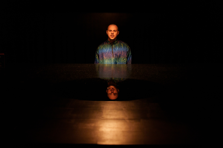 Un homme debout avec un imperméable multicolore se tient au-dessus d'une surface lisse qui réfléchit son visage.