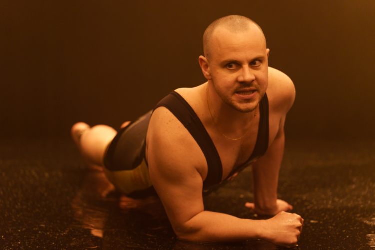 Un homme en tenue de cycliste noire est en position de gainage au sol, illuminé par une lumière sépia.