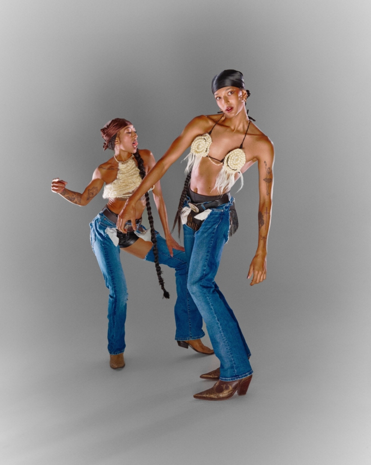 Posant l'une devant l'autre, Stacey et Satinée mettent en valeur leurs longues tresses et leurs habits de cowboy : short en cuir noir, chaps en jeans, bottes de cowboy et haut en corde blanche.