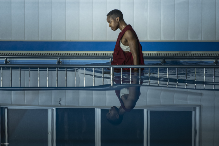 L'artiste Dana Michel entre dans une piscine vêtue d'un gilet rouge et son buste se reflète dans l'eau.
