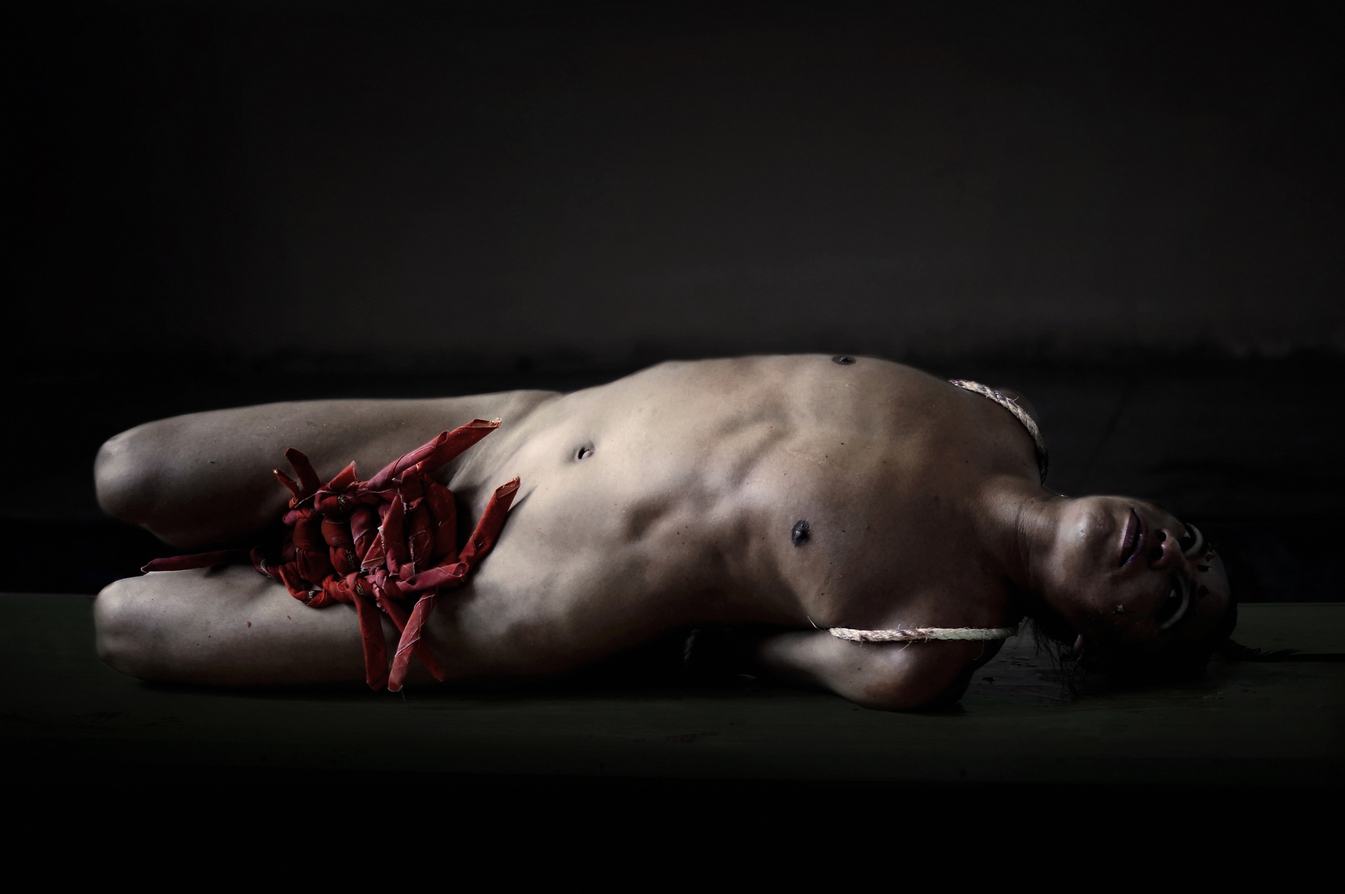 Lukas Avendano est allongé nu sur son flanc gauche alors que son entrejambe est recouvert de morceaux de tissu rouges.