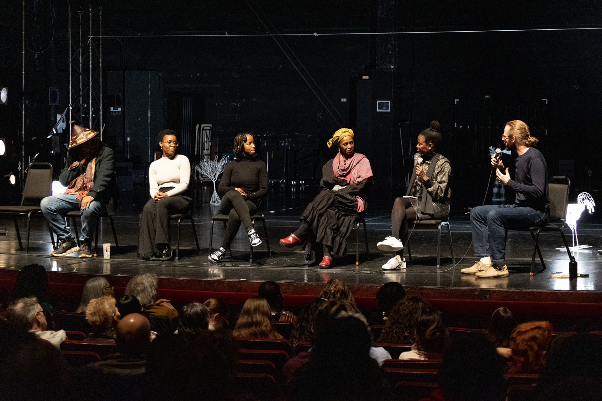 Plusieurs artistes sont assis sur des chaises sur scène, accompagnés d'un modérateur, pour discuter avec le public du spectacle.