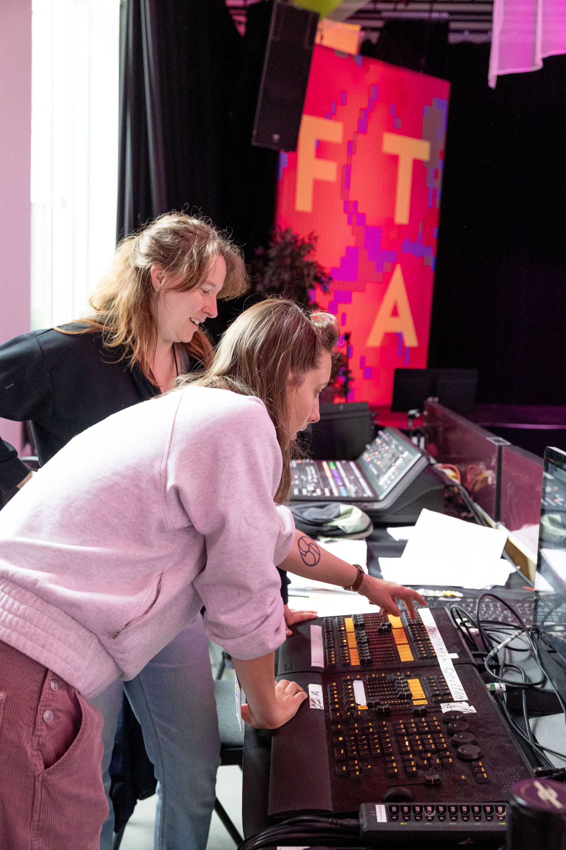 Deux personnes sont penchées au-dessus d'une table de régie, l'une montrant à l'autre comment elle fonctionne.