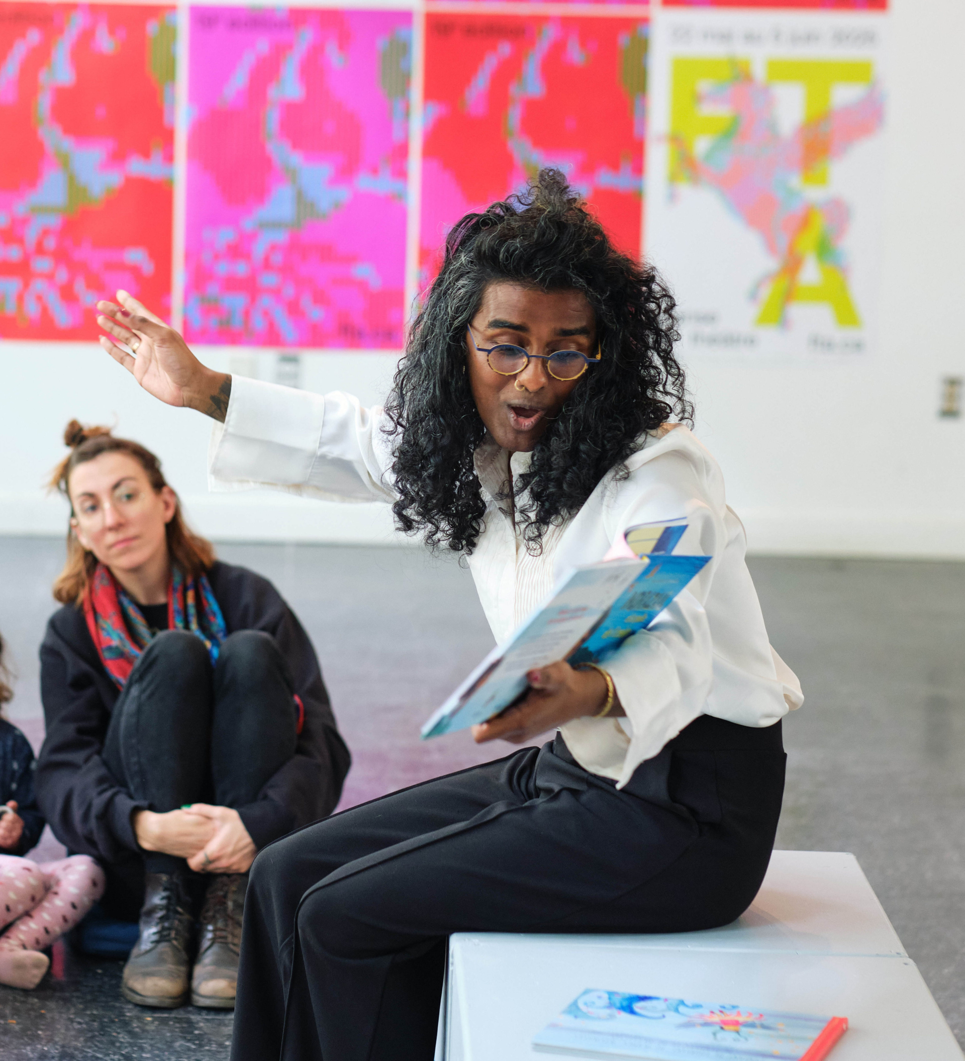 Kama La Mackerel tient un livre pour enfant dans les mains et en fait la lecture à des enfants.
