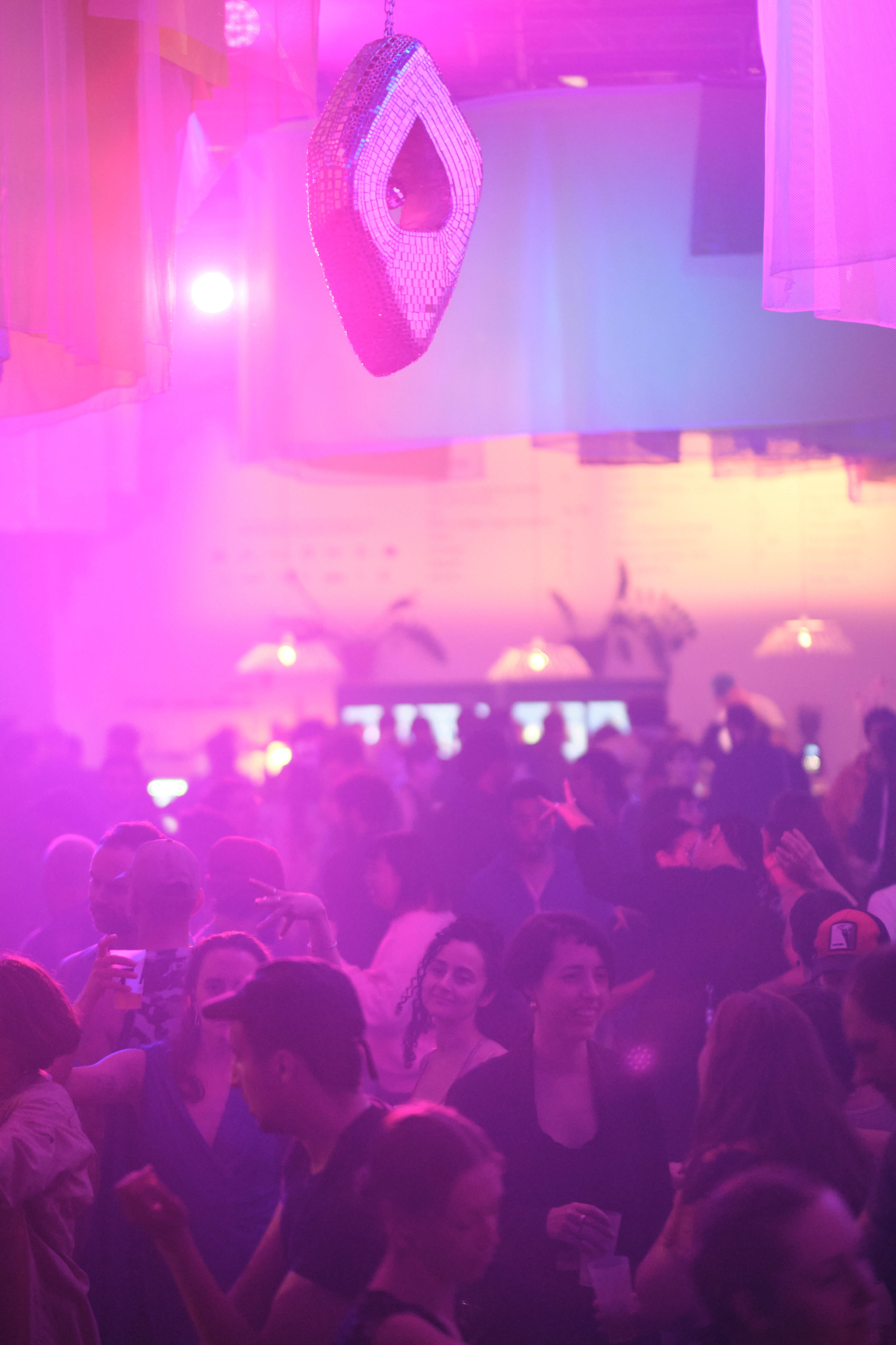 Many people are dancing in a room lit up in pink.