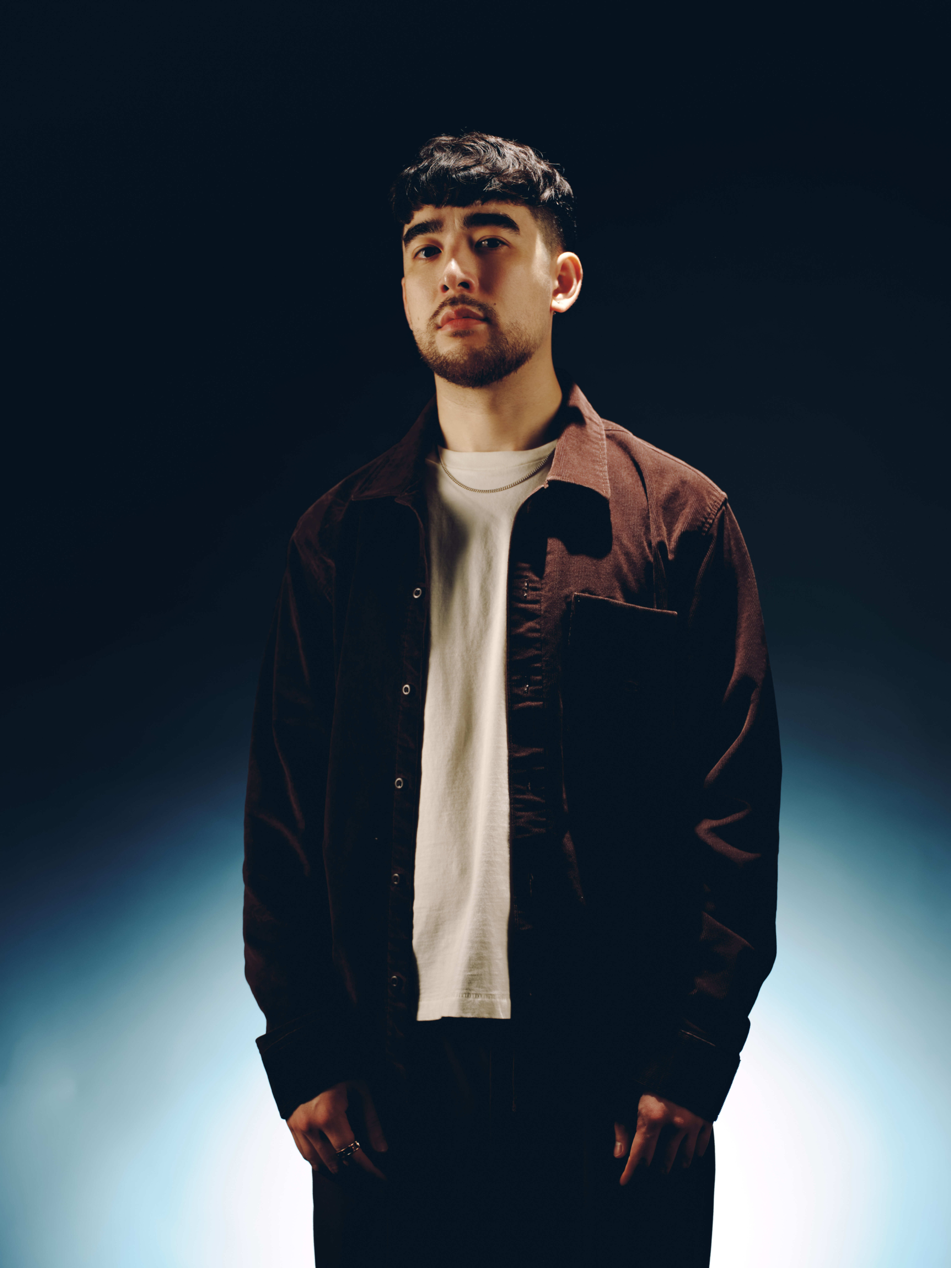 A portrait of DJ Tdesu wearing a brown jacket over a beige T-shirt.