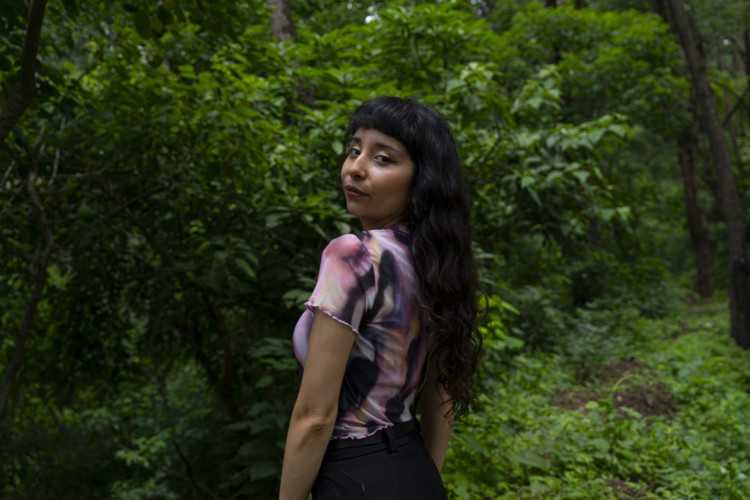 L’artiste chilienne Taina Villalobos se tient devant une forêt à la végétation dense et vert lumineux.