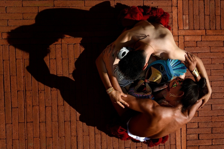 Deux personnes torses nus se tiennent par leurs bras qui forment un cercle et se penchent au-dessus d'un masque posé au sol.
