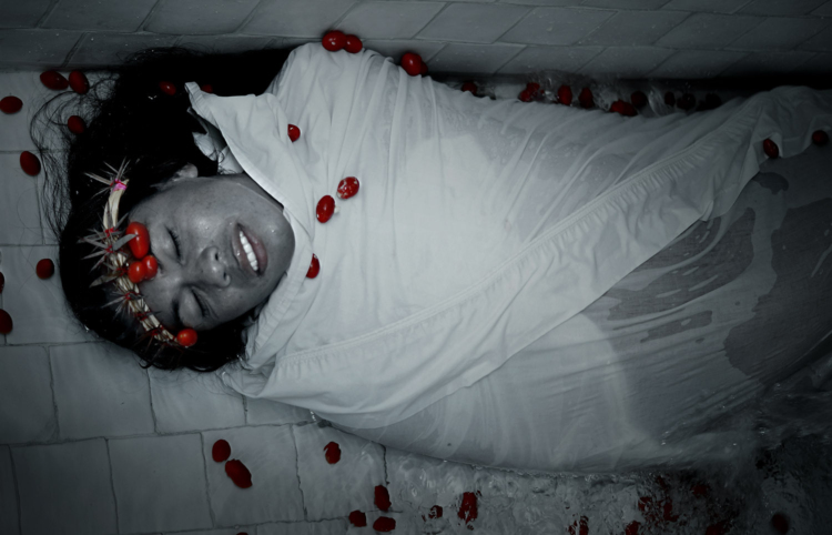 Lukas Avendano, portant une sorte de couronne avec des épines, est enroulé dans un tissu blanc imprégné d'eau, comme un linceul, et allongé sur un carrelage avec de l'eau.