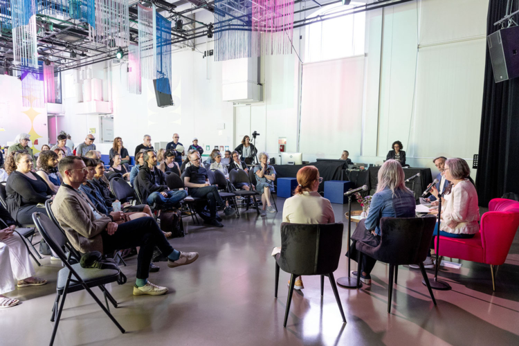 Une assemblée de personnes assises écoutent un groupe de conférenciers.