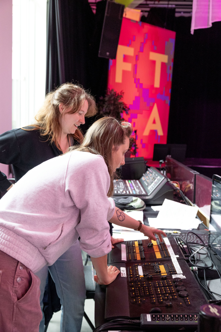 Deux personnes sont penchées au-dessus d'une table de régie, l'une montrant à l'autre comment elle fonctionne.