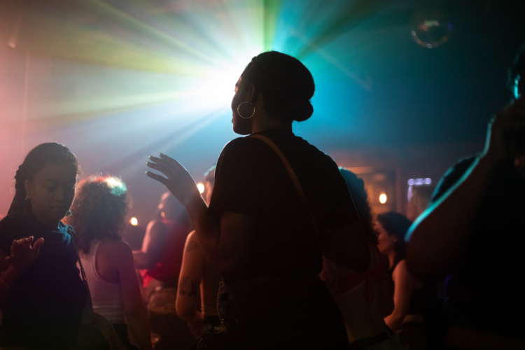 Une silhouette d'une personne qui danse se distingue grâce à un effet de contre-jour avec le flash de projecteurs dans une soirée festive en intérieur.