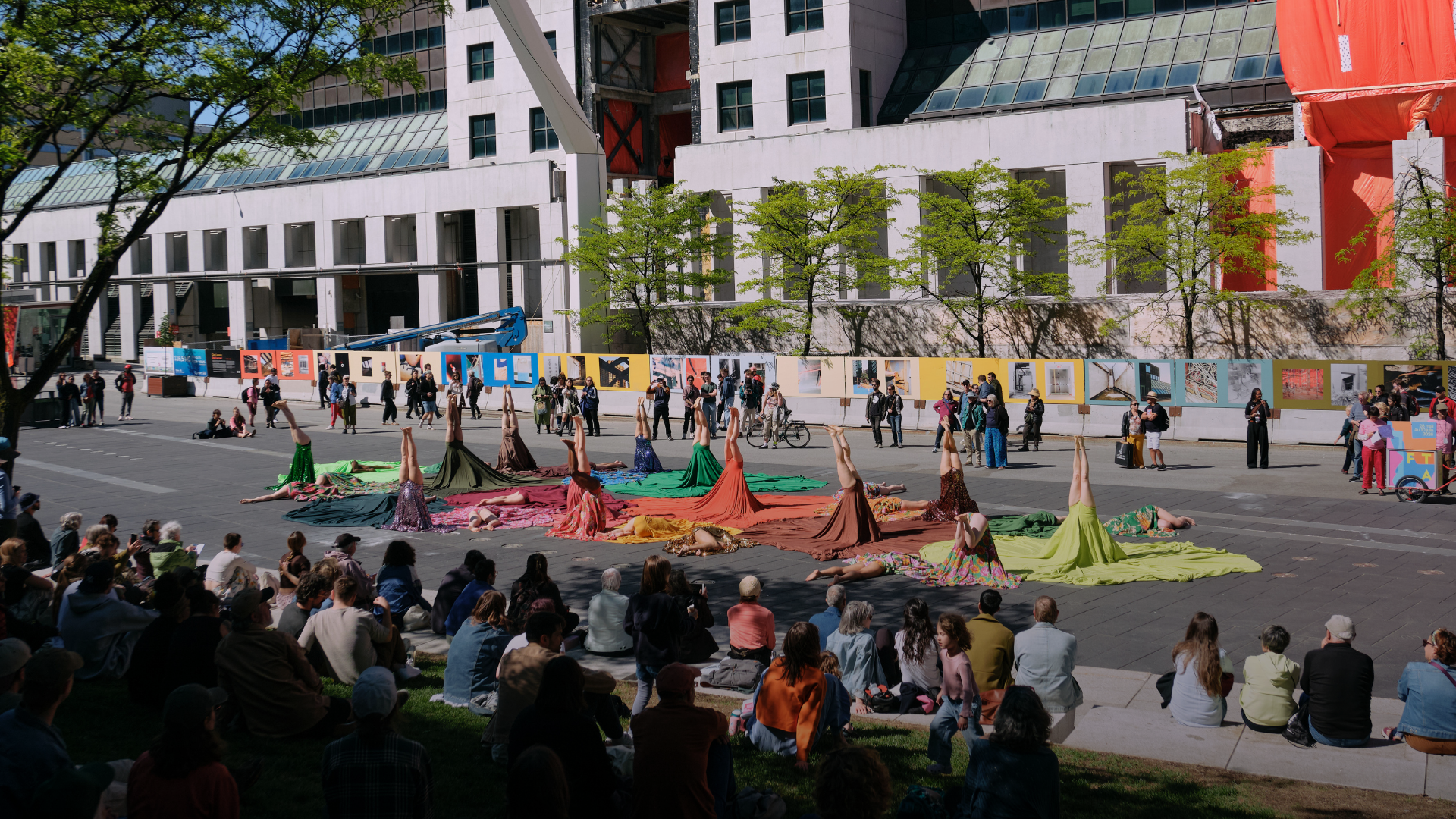 About twenty people are doing handstands on Montreal's Place des Festivals while wearing large, colorful skirts that form circles on the ground.