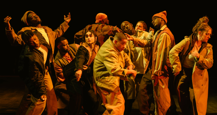 Dans un espace restreint, dix danseurs et danseuses sont en mouvement sous un éclairage orangé.